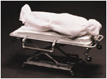 a corpse wrapped in a  white sheet on a gurney